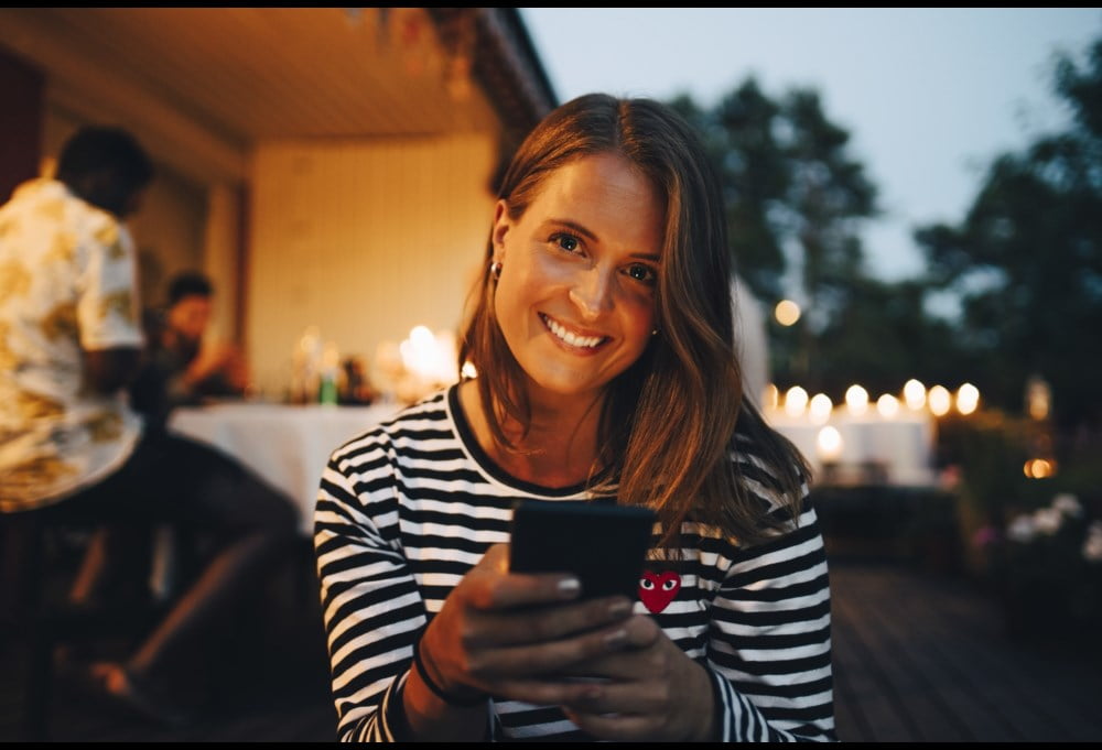 Dame med mobil smiler til kamera